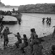 Survivors from HMS Sir Galahad (ablaze in the background) are hauled ashore by colleagues at Bluff Cove, East Falkland, after the ship was hit by an Argentinian air attack on June 29, 1982, during the Falklands conflict